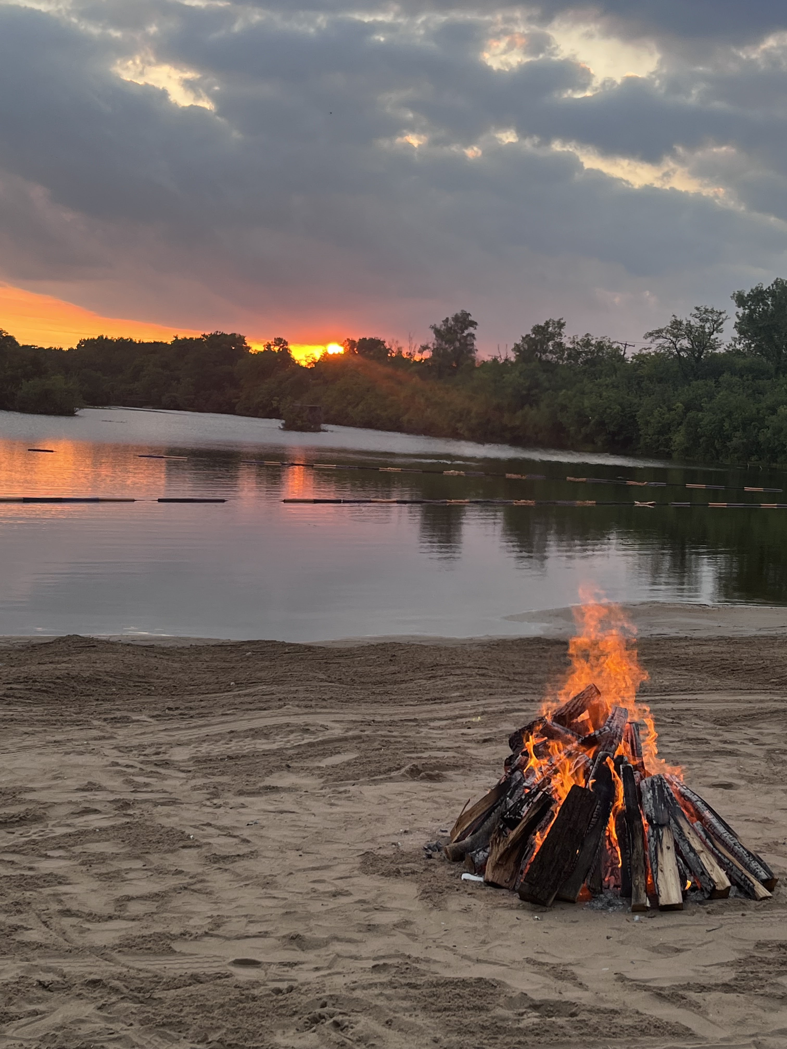 Campfire burning on the sandy beach at Deer Creek Lake during a vivid sunset