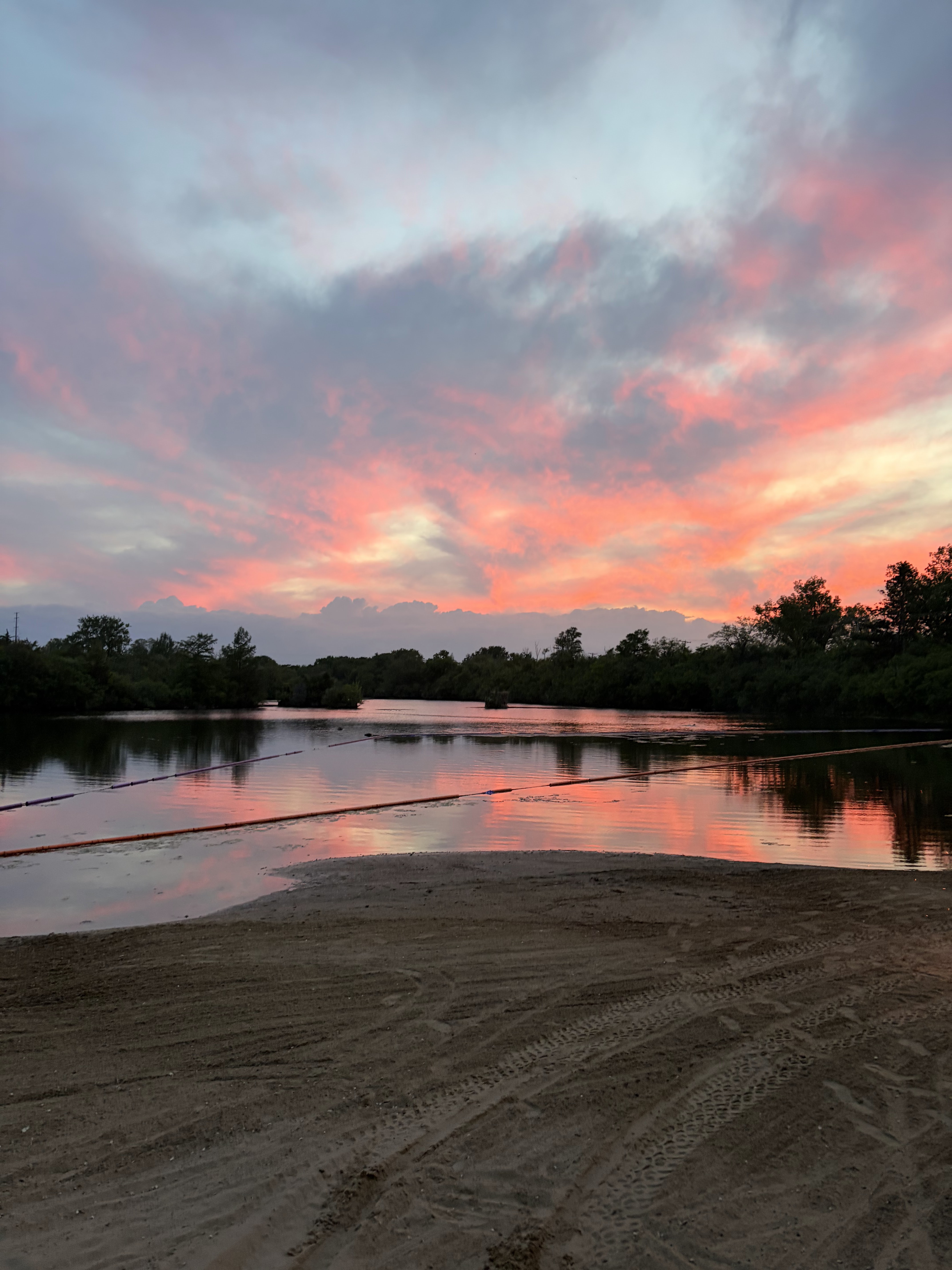 Pink and orange sunset sky reflected over the private beach at Deer Creek Lake in Plainfield Illinois