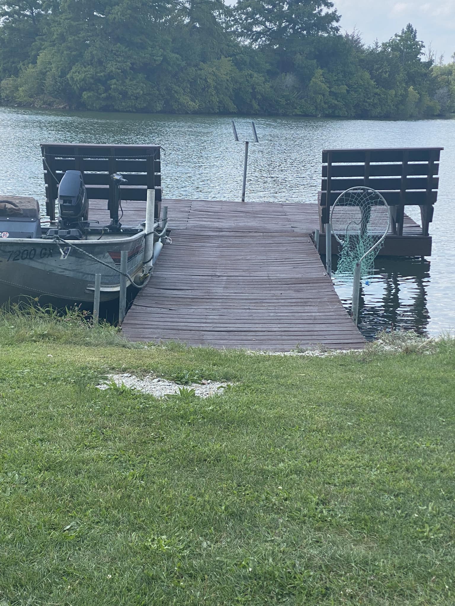 Wooden boat dock with fishing boat moored on Deer Creek Lake with wooded island in background