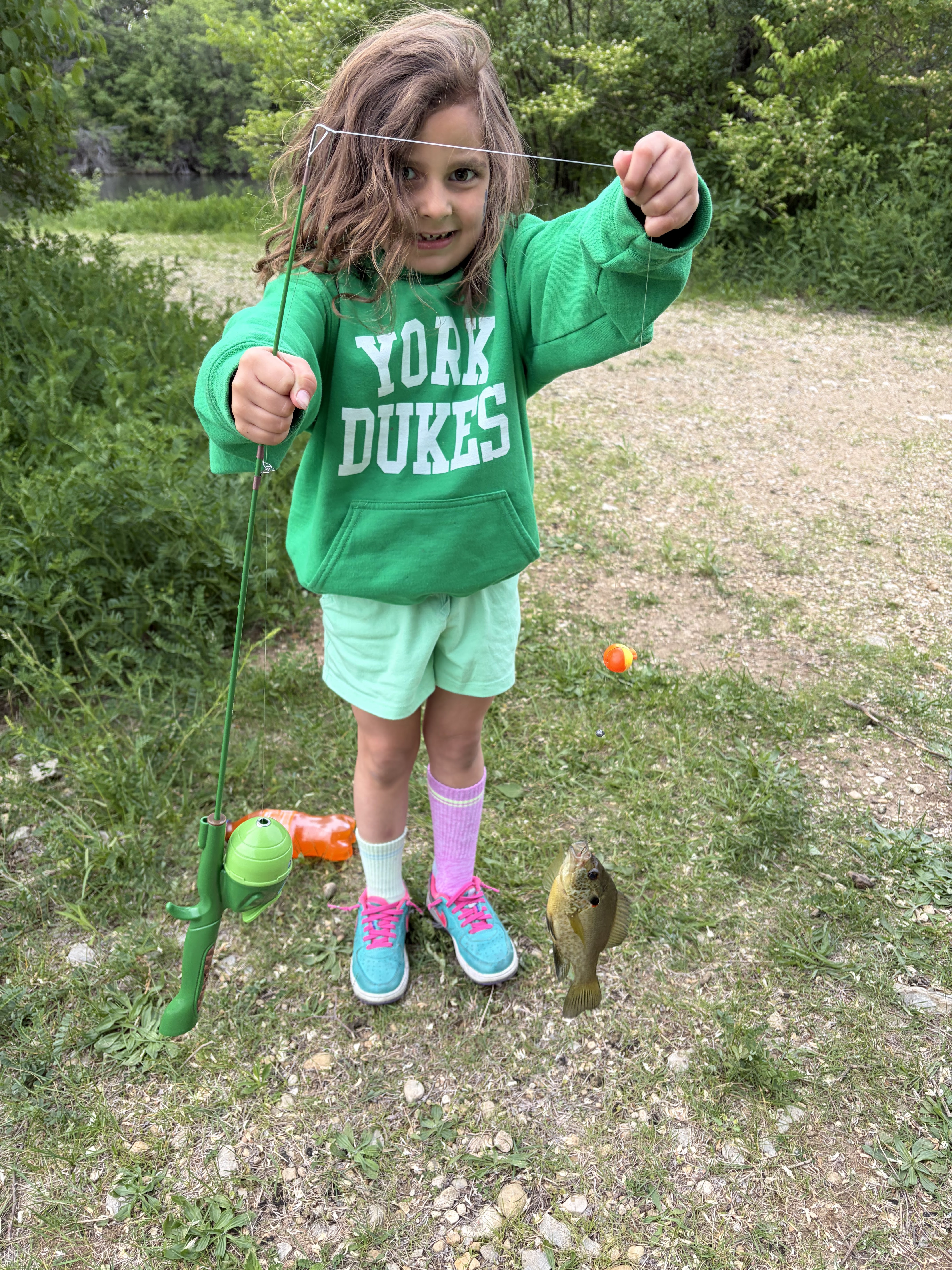 Young girl proudly holding her first bluegill catch while fishing at Deer Creek Recreation Club
