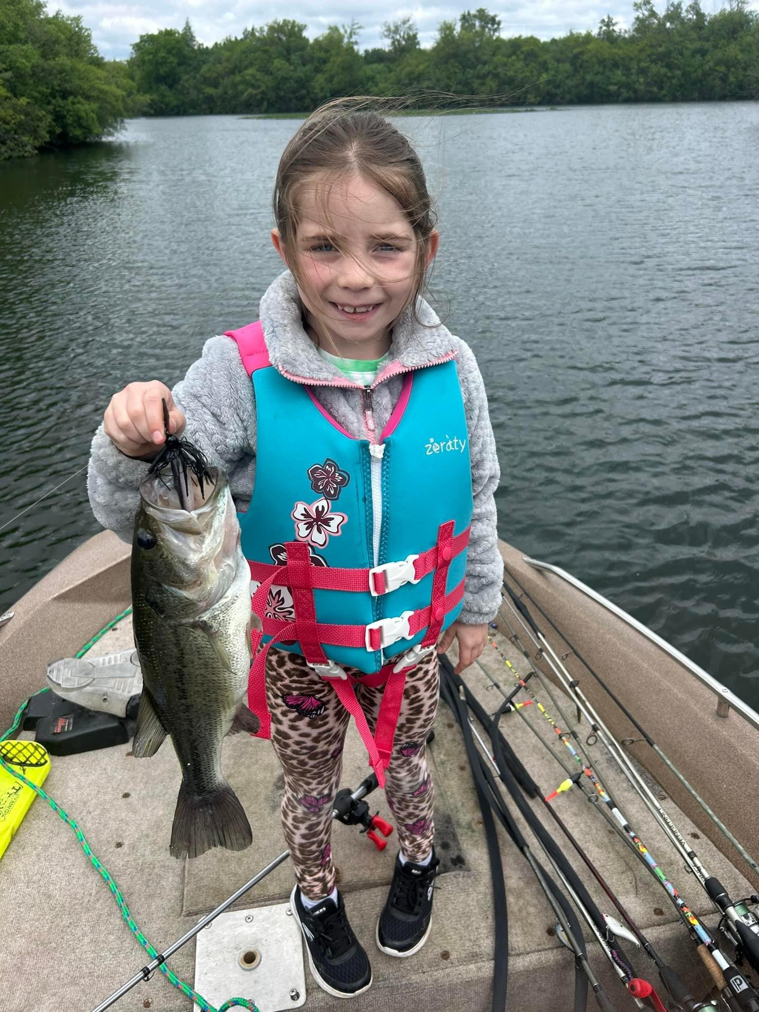 Young girl in life jacket proudly holding a largemouth bass caught on Deer Creek Lake