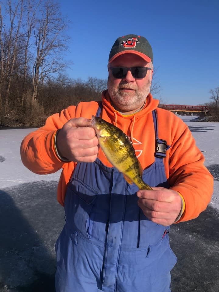 Club member holding a yellow perch caught ice fishing on a frozen Deer Creek Lake in winter