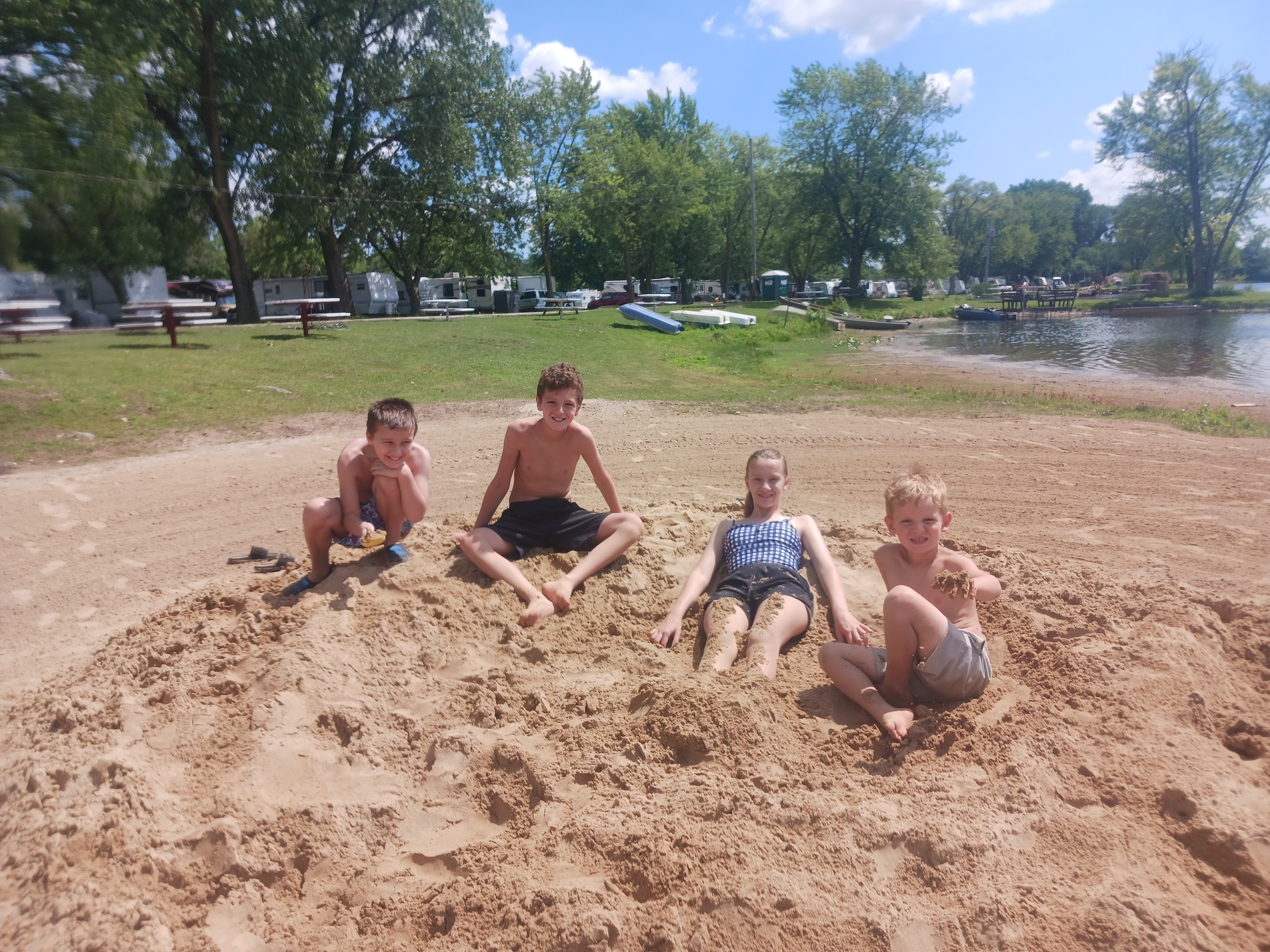 Four kids playing and burying themselves in the sand on the private beach at Deer Creek Recreation Club